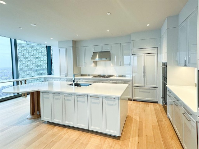 kitchen with a center island with sink, sink, paneled refrigerator, light hardwood / wood-style floors, and stainless steel gas cooktop