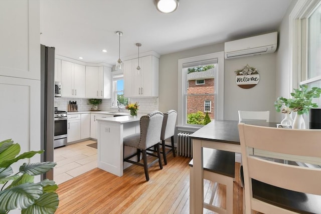 475 E St, Dedham, MA 02026 - kitchen with stainless steel appliances, an AC wall unit, a breakfast bar area, decorative backsplash, and white cabinets