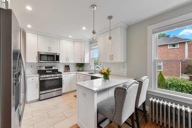 475 E St, Dedham, MA 02026 - kitchen featuring radiator heating unit, appliances with stainless steel finishes, a peninsula, light countertops, and white cabinets
