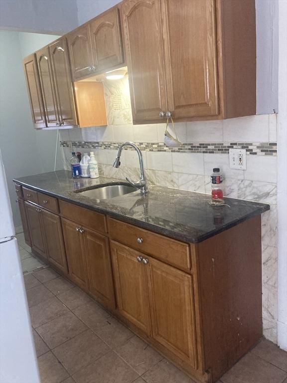 kitchen featuring tasteful backsplash, sink, dark stone counters, and light tile patterned flooring