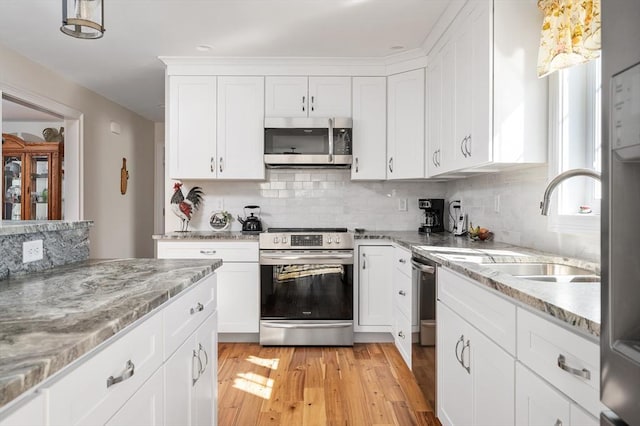 kitchen with stainless steel appliances, white cabinetry, decorative backsplash, and light wood finished floors