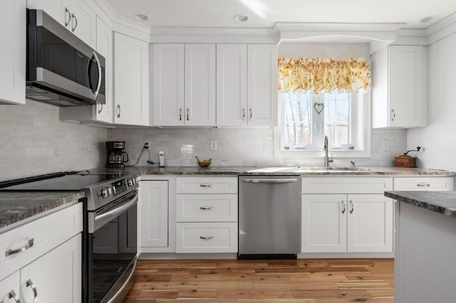 kitchen featuring dark stone counters, appliances with stainless steel finishes, light wood-style flooring, and white cabinetry