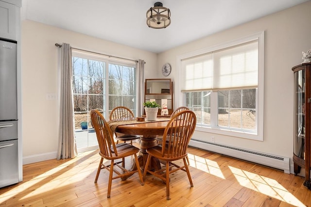 dining area featuring a baseboard radiator, baseboards, and light wood finished floors