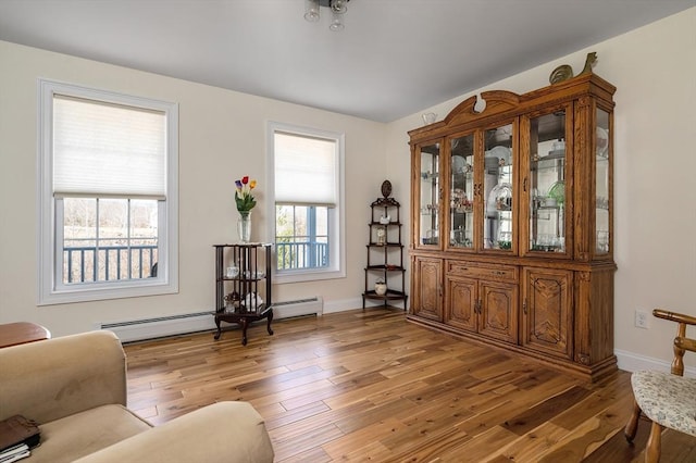 living area with a baseboard heating unit, light wood-style flooring, and baseboards