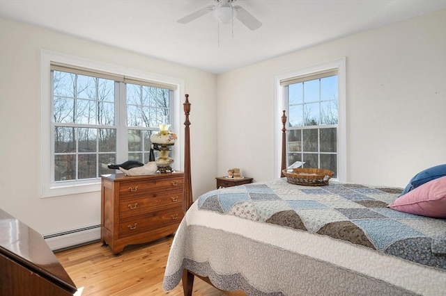 bedroom featuring light wood-style flooring, multiple windows, a ceiling fan, and a baseboard radiator