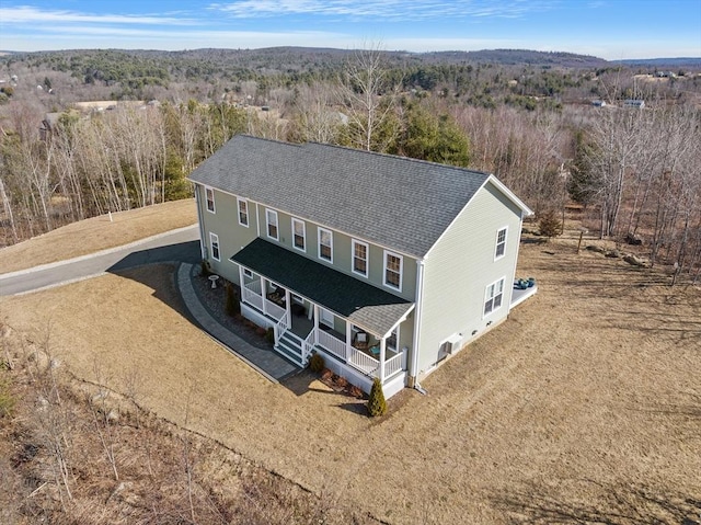 view of front facade featuring covered porch, driveway, a forest view, and a shingled roof