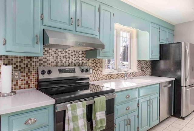 kitchen featuring blue cabinetry, stainless steel appliances, light countertops, under cabinet range hood, and a sink