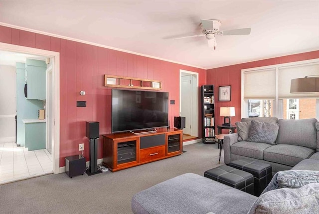 living area featuring carpet floors, baseboards, ornamental molding, and a ceiling fan