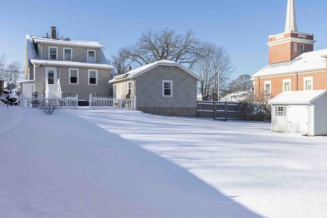 snow covered property featuring a fenced front yard, a chimney, and an outdoor structure