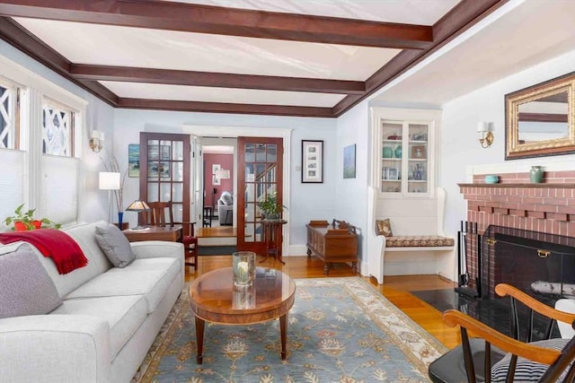 living room featuring baseboards, wood finished floors, french doors, a brick fireplace, and beam ceiling