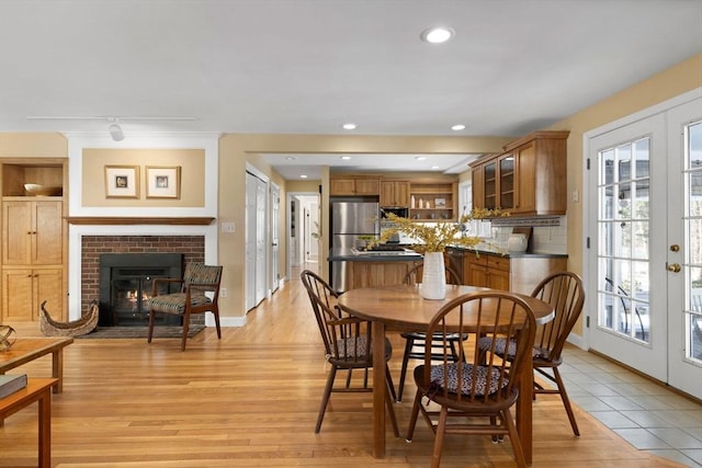 dining space featuring a brick fireplace, light wood-type flooring, and french doors