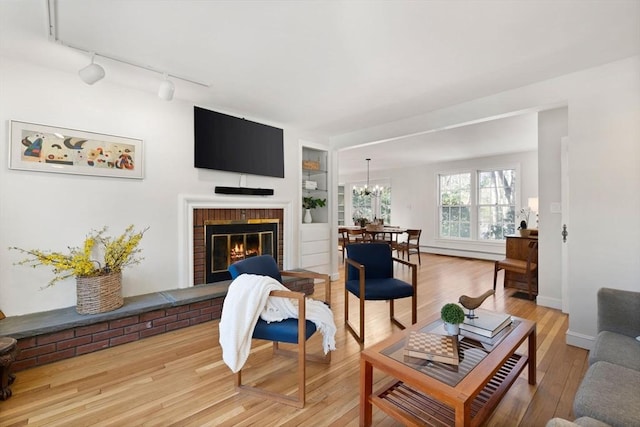 living room featuring hardwood / wood-style flooring, a brick fireplace, track lighting, an inviting chandelier, and built in shelves