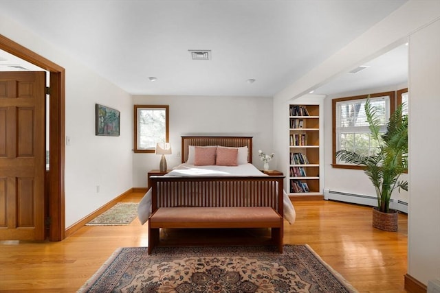 bedroom featuring multiple windows, a baseboard heating unit, and light hardwood / wood-style floors