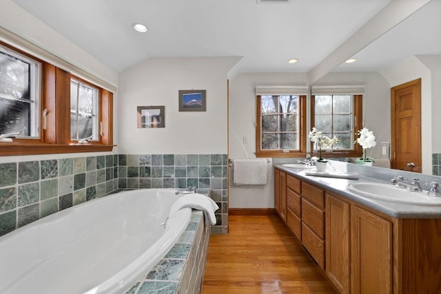 bathroom featuring vanity, lofted ceiling, wood-type flooring, and a relaxing tiled tub