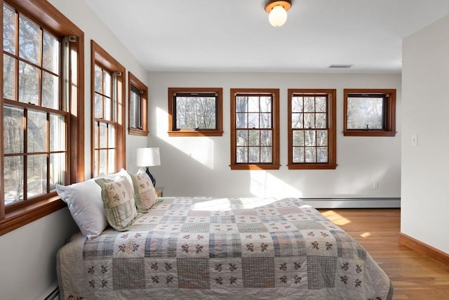 bedroom with multiple windows, a baseboard heating unit, and light hardwood / wood-style floors