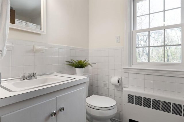 bathroom with vanity, toilet, radiator, and tile walls