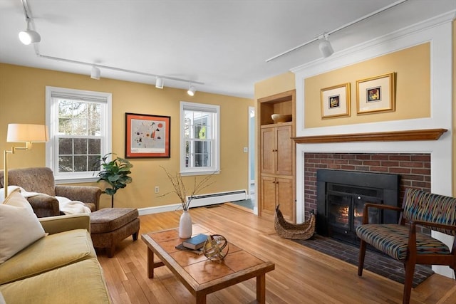 living room featuring a baseboard radiator, a fireplace, rail lighting, and light wood-type flooring