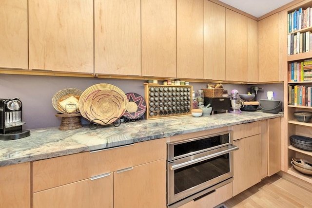 kitchen with light stone counters, light wood finished floors, stainless steel oven, and light brown cabinetry