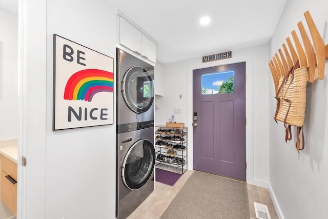 clothes washing area with baseboards, laundry area, stacked washer / dryer, and visible vents