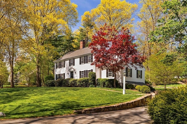 colonial home featuring a chimney and a front yard