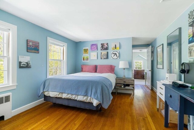 bedroom featuring multiple windows, wood finished floors, radiator, and baseboards