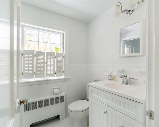 bathroom with radiator, tile walls, toilet, vanity, and a wainscoted wall