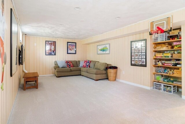 carpeted living room featuring baseboards, wood walls, and ornamental molding