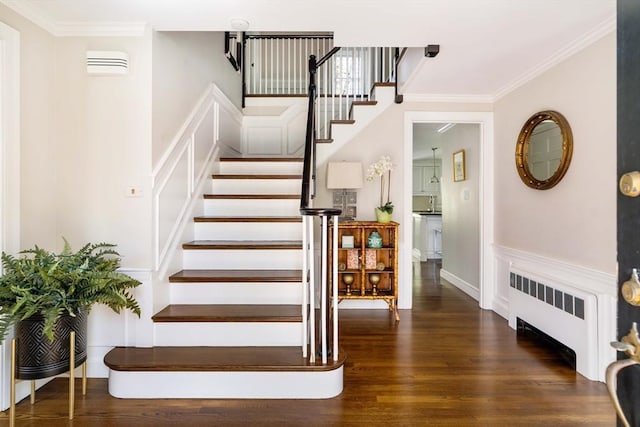 staircase featuring radiator, wood finished floors, crown molding, a wainscoted wall, and a decorative wall