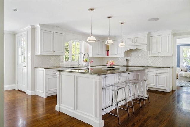 kitchen with dark wood-type flooring, backsplash, white cabinetry, a kitchen island with sink, and a sink