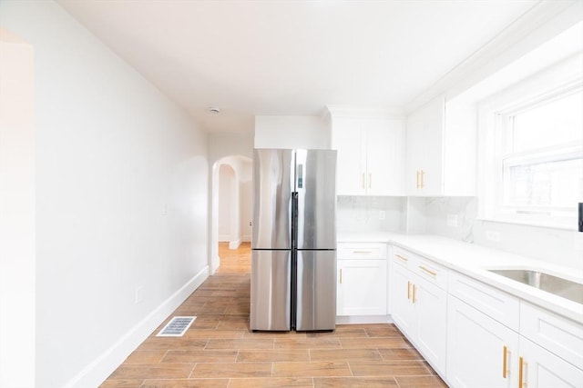 kitchen with arched walkways, freestanding refrigerator, light countertops, white cabinetry, and visible vents