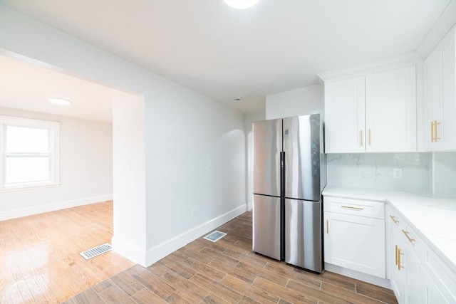 kitchen with baseboards, freestanding refrigerator, light wood finished floors, white cabinetry, and visible vents