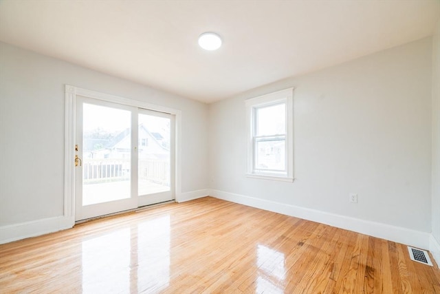 empty room featuring light wood finished floors, visible vents, a wealth of natural light, and baseboards
