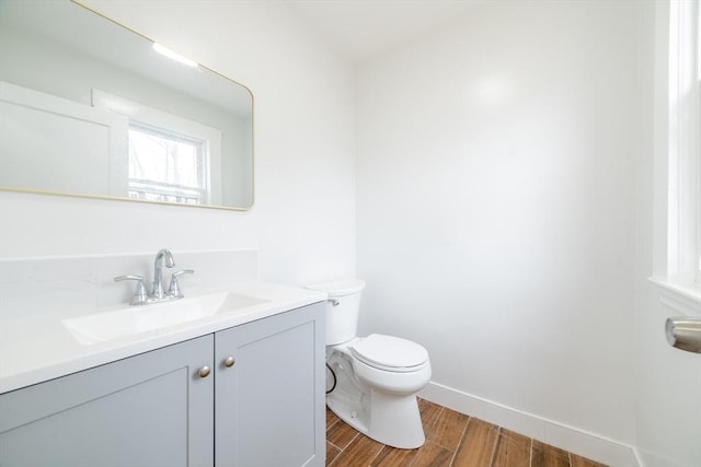 half bath with baseboards, wood finished floors, toilet, and vanity