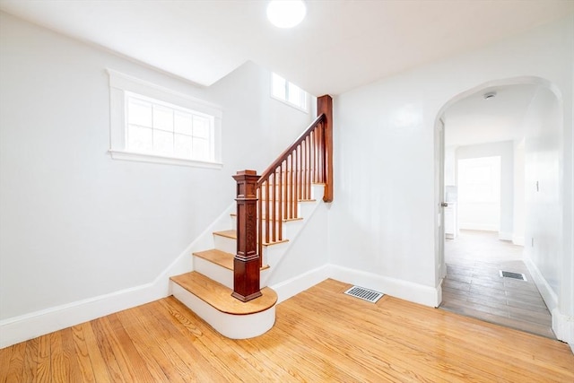 staircase featuring arched walkways, visible vents, wood finished floors, and baseboards