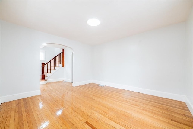 empty room featuring baseboards, light wood-type flooring, arched walkways, and stairs