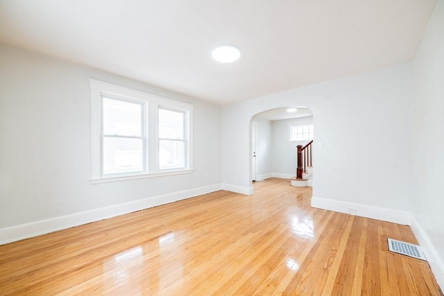 empty room with stairway, visible vents, baseboards, arched walkways, and light wood-type flooring