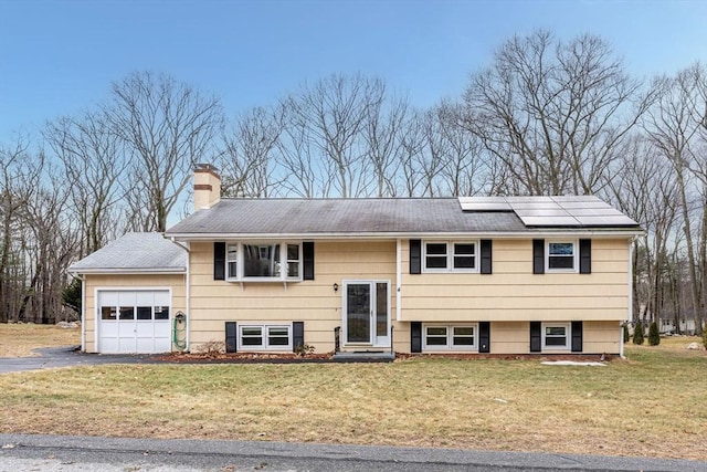 split foyer home with solar panels, a chimney, a front lawn, a garage, and aphalt driveway