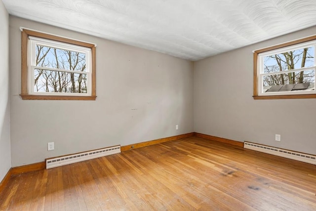 spare room with baseboard heating, a healthy amount of sunlight, and light wood finished floors