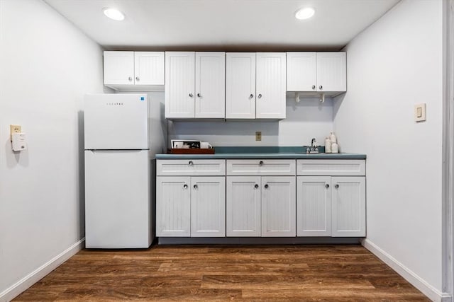 kitchen featuring baseboards, dark wood-style flooring, freestanding refrigerator, and a sink