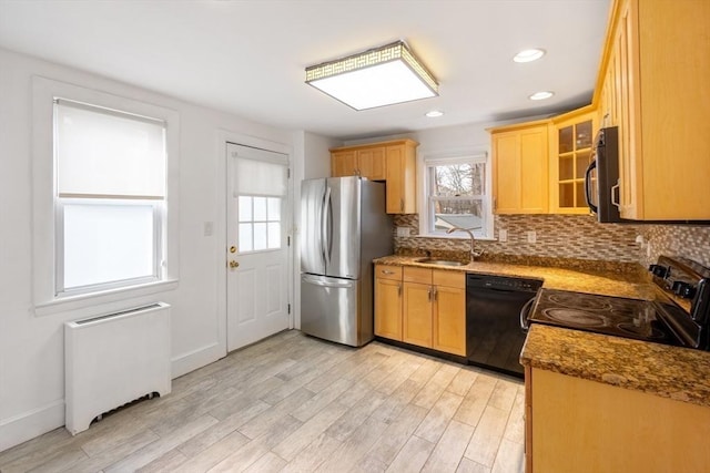 kitchen with stone countertops, radiator heating unit, sink, black appliances, and light hardwood / wood-style flooring