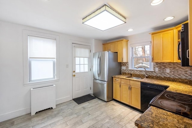 kitchen featuring sink, stainless steel refrigerator, dishwasher, radiator heating unit, and dark stone counters