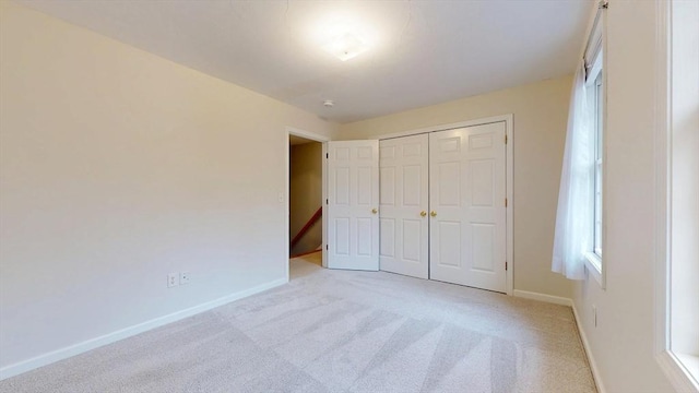 unfurnished bedroom with baseboards, a closet, and light colored carpet