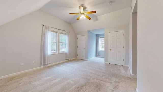 unfurnished bedroom featuring light carpet, baseboards, lofted ceiling, and a ceiling fan
