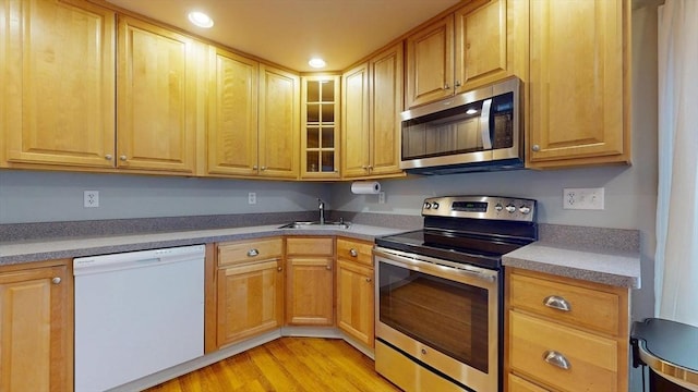 kitchen featuring a sink, glass insert cabinets, stainless steel appliances, light wood-style floors, and recessed lighting