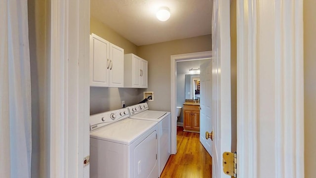 laundry area with independent washer and dryer, light wood-style flooring, and cabinet space