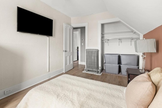 bedroom with radiator, baseboards, lofted ceiling, and wood finished floors