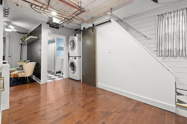 clothes washing area featuring laundry area, stacked washer / drying machine, a barn door, and hardwood / wood-style flooring