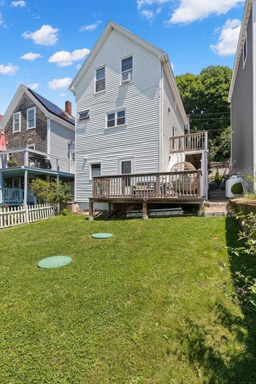 rear view of property with a lawn, a wall mounted air conditioner, a deck, and fence