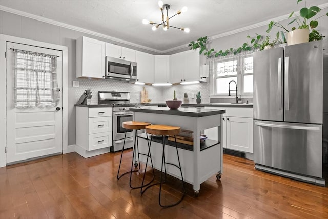 kitchen featuring dark wood-style flooring, ornamental molding, stainless steel appliances, white cabinets, and dark countertops