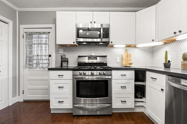 kitchen featuring dark countertops, crown molding, dark wood-style floors, white cabinets, and stainless steel appliances